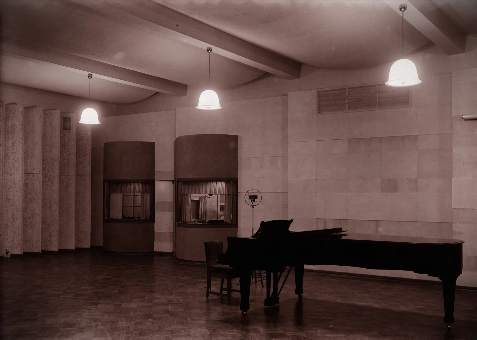 A grand piano in a 1930s radio studio with pendant lamps.